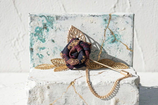 Broche épingle Roaring 20s Paris en forme de rose, tissu à carreaux bordeaux et bleu marine, avec chaîne et feuilles dorées.