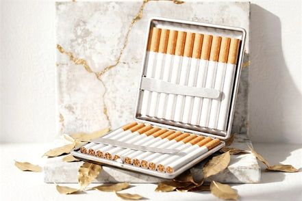 Étui à cigarettes Roaring 20s Paris en métal argenté, contenant 20 cigarettes, ouvert sur un fond marbre doré et feuilles dorées.