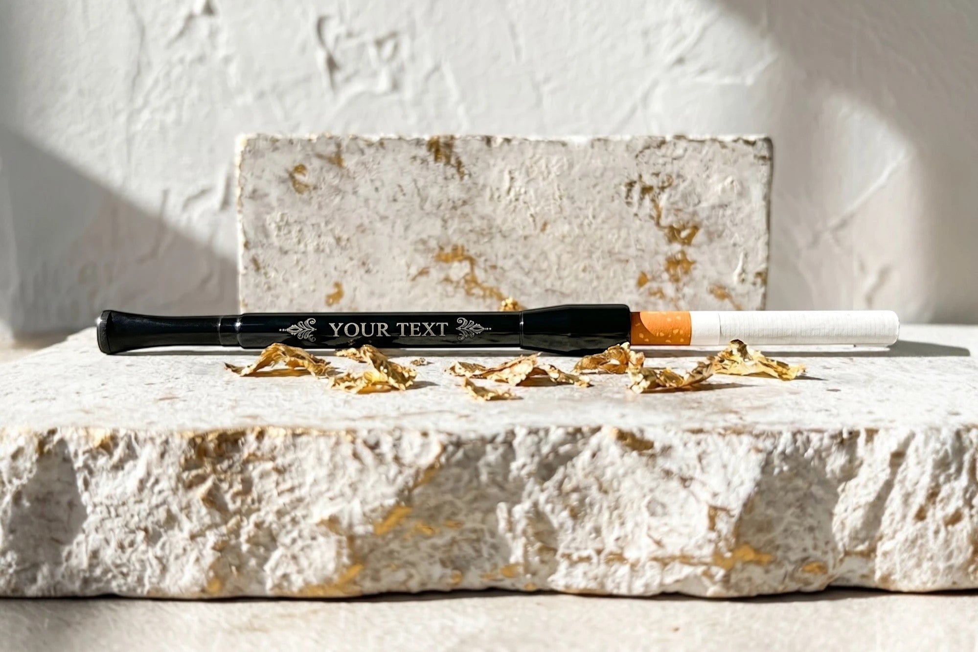 Porte-cigarette noir en aluminium inoxydable avec gravure personnalisée et cigarette orange et blanche. Roaring 20s Paris.